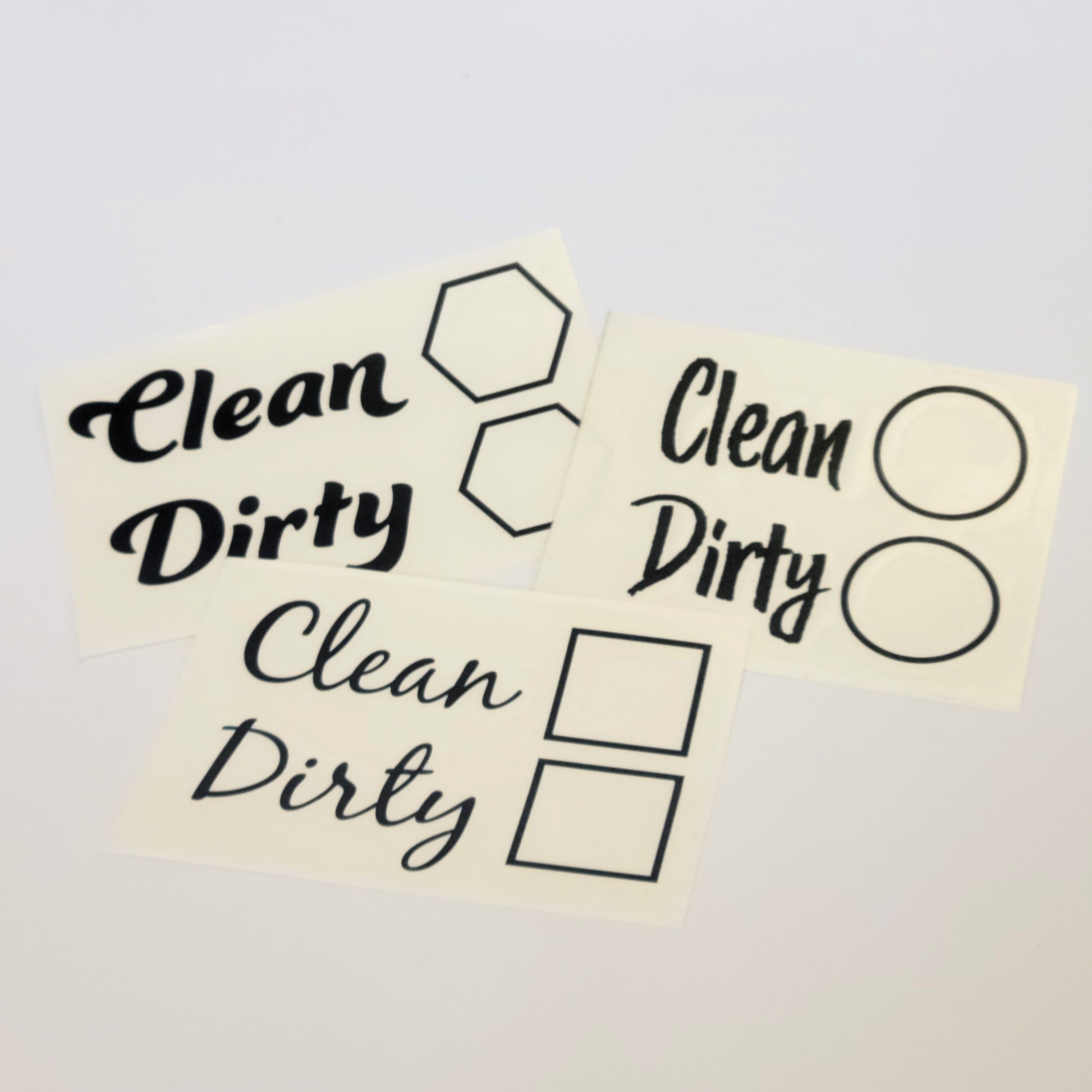 The InkBird Print Studio LLC Clean/Dirty Dishwasher Vinyl Cut Decal serves as a clever chore reminder with stickers featuring the words "Clean" and "Dirty" in various fonts. Accompanying these words are dishwasher decal icons such as hexagons, circles, and squares, all crafted from durable vinyl with permanent adhesive for lasting use.
