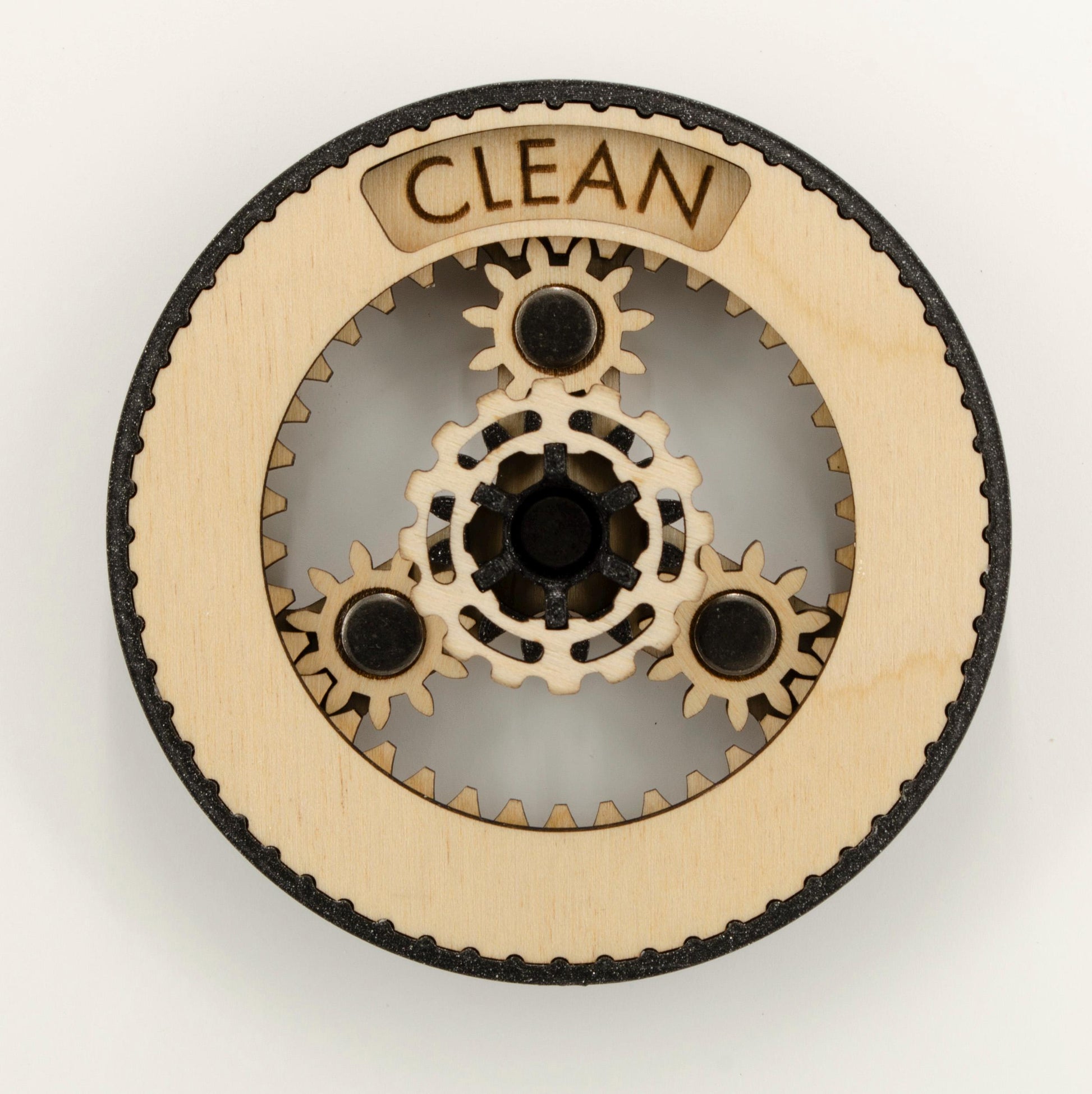 A round dishwasher magnet with rotating planetary gears made of laser-cut wood, enclosed in a 3D-printed PLA housing. The gears can be rotated to reveal either 'CLEAN' or 'DIRTY' in an engraved display window at the top, indicating the dishwasher's status.