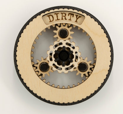 A round dishwasher magnet with rotating planetary gears made of laser-cut wood, enclosed in a 3D-printed PLA housing. The gears move to reveal either 'CLEAN' or 'DIRTY' in an engraved display window at the top, indicating the dishwasher's status.