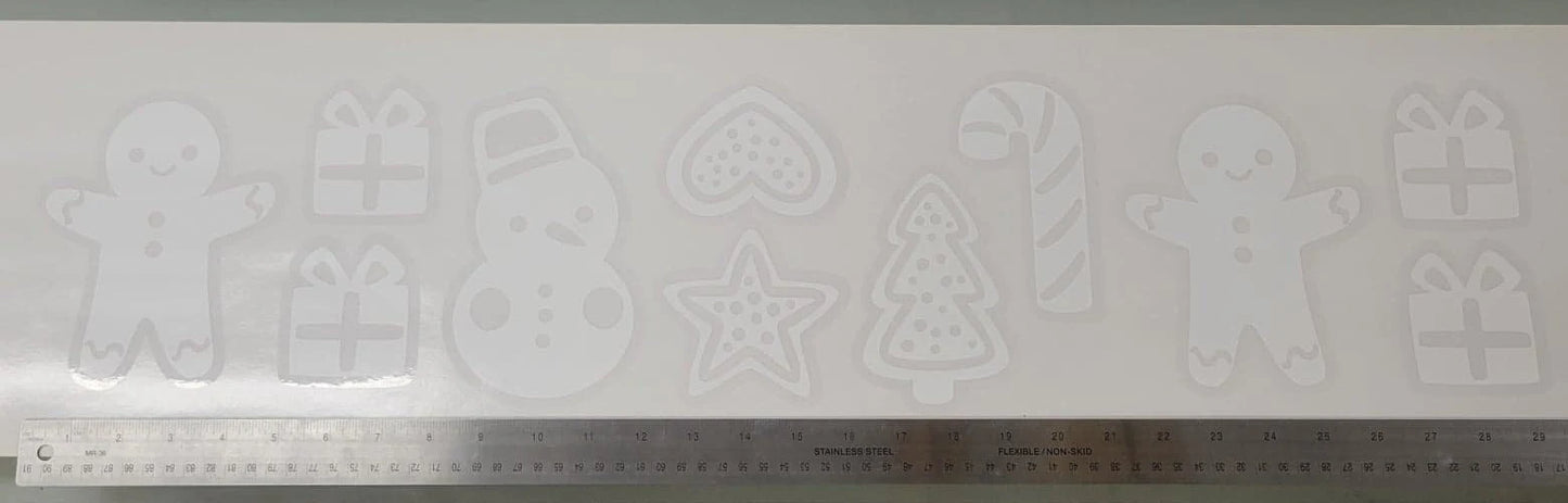 The Holiday Cookie Static Cling Set by InkBird Print Studio LLC features a collection of cookie cutter designs such as a gingerbread man, snowman, heart, star, Christmas tree, and candy cane. It's perfect for creating festive window decorations and includes gift box designs. A ruler at the bottom helps indicate the scale of these renter-friendly winter window clings.