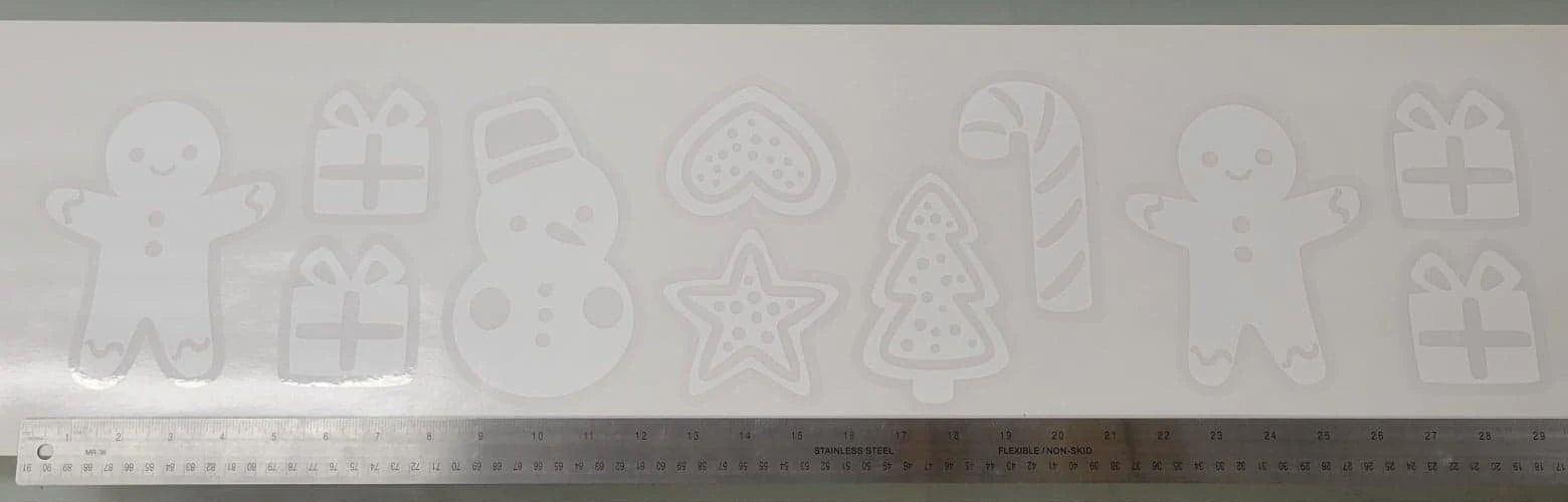The Holiday Cookie Static Cling Set by InkBird Print Studio LLC features a collection of cookie cutter designs such as a gingerbread man, snowman, heart, star, Christmas tree, and candy cane. It's perfect for creating festive window decorations and includes gift box designs. A ruler at the bottom helps indicate the scale of these renter-friendly winter window clings.