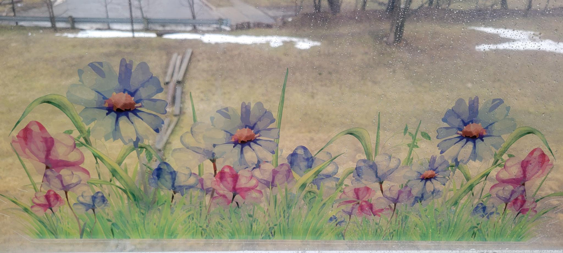 decorative floral design of a meadow, static cling, applied to a rainy window. Blues and pinks, stained glass or watercolor vibes, a grassy field is shown outside the window
