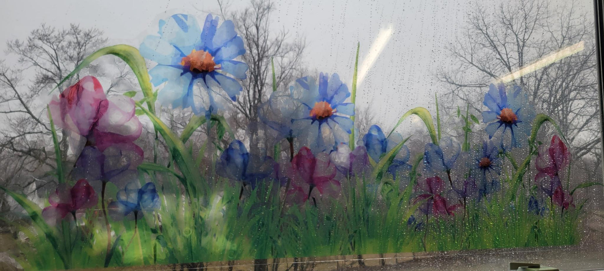 decorative floral design of a meadow, static cling, applied to a rainy window. Blues and pinks, stained glass or watercolor vibes
trees can be seen through the imagery, blurry but visible
