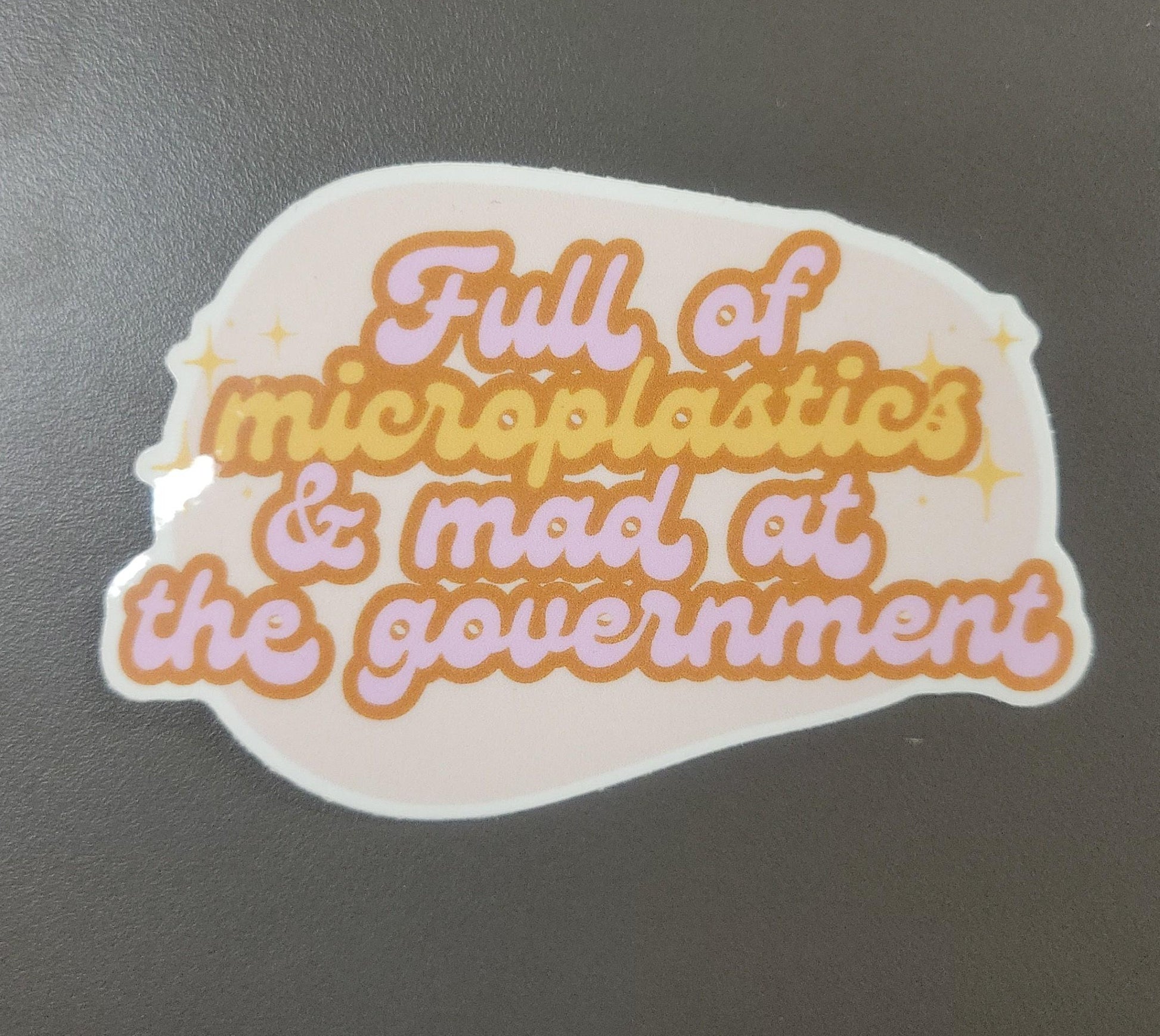 Sticker with text 'Full of microplastics & mad at the government' on a dark background
