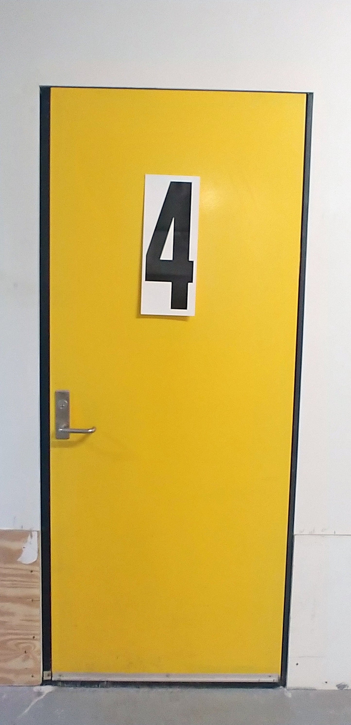 An 18 inch tall decal with the number 4 on it, black ink on white matte vinyl, applied to a yellow door.
