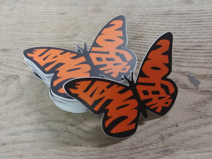 A stack of decals in the shape of a monarch butterfly. The wings, instead of the usual shapes of a Monarch, spell out the words "No Hate" and "No Fear" in orange. The text is bold and stands out against the design, emphasizing a message of peace and positivity. This is a pro-immigration decal.