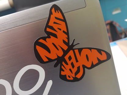 Our No Hate No Fear Butterfly applied to a laptop case. This decal is in the shape of a monarch butterfly. The wings, instead of the usual shapes of a Monarch, spell out the words "No Hate" and "No Fear" in orange. The text is bold and stands out against the design, emphasizing a message of peace and positivity. This is a pro-immigration decal.