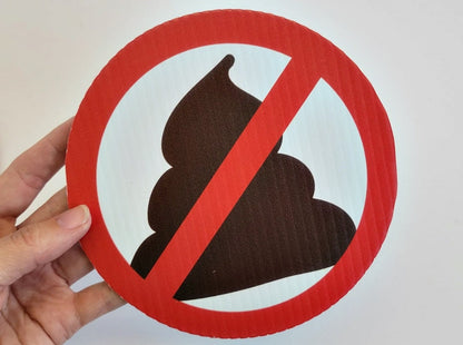 A closeup photo of our no pooping yard sign in a hand, showing it's size and scale. it is 6 inches in diameter. A poop emoji shape with a red circle and slash through it.