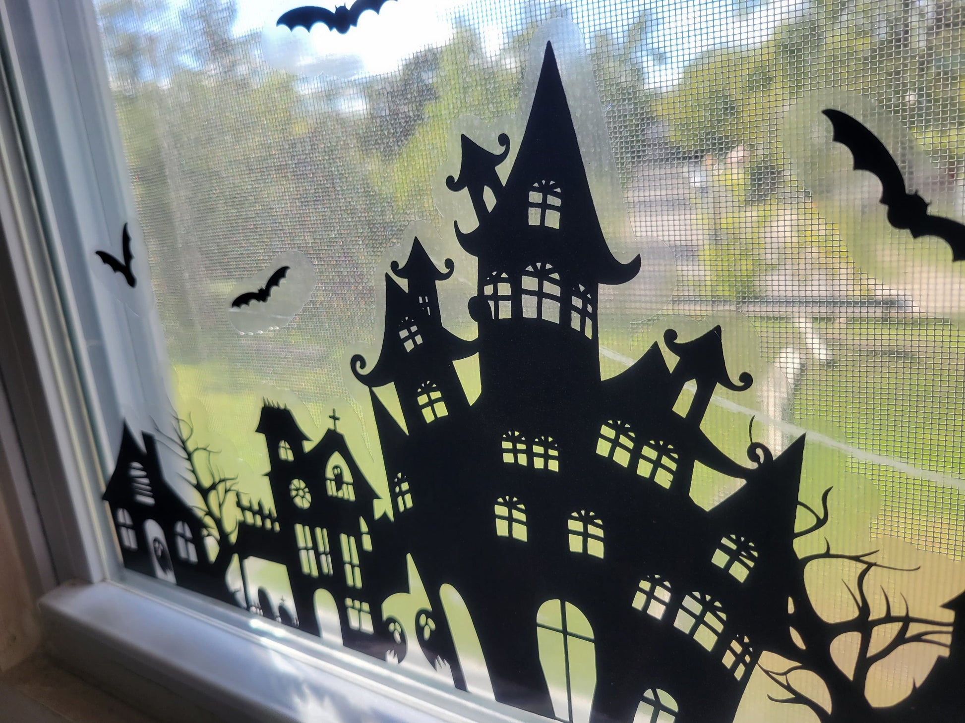 A closeup shot of part of our Our Spooky Town Halloween static cling window decoration. Black ink on a clear material, applied to a window with a sunny exterior seen in the background.
