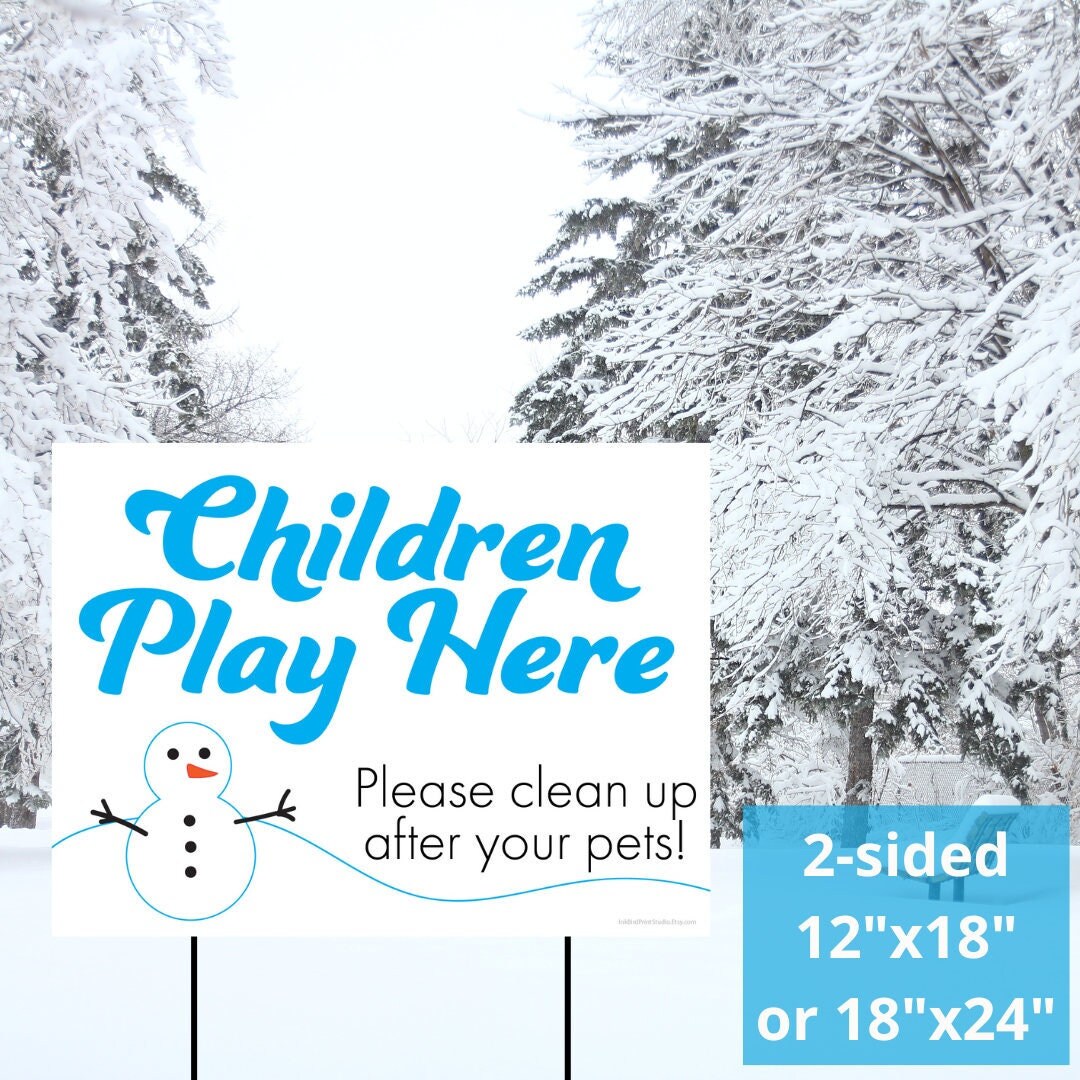 In a snowy landscape, an InkBird Print Studio LLC yard sign titled "Children Play Here Please Clean Up After Your Pets" is displayed, featuring blue text for the message and a cheerful snowman illustration. The double-sided sign, available in 12"x18" or 18"x24" sizes with other custom sizes upon request, is set amidst the snow-covered trees.