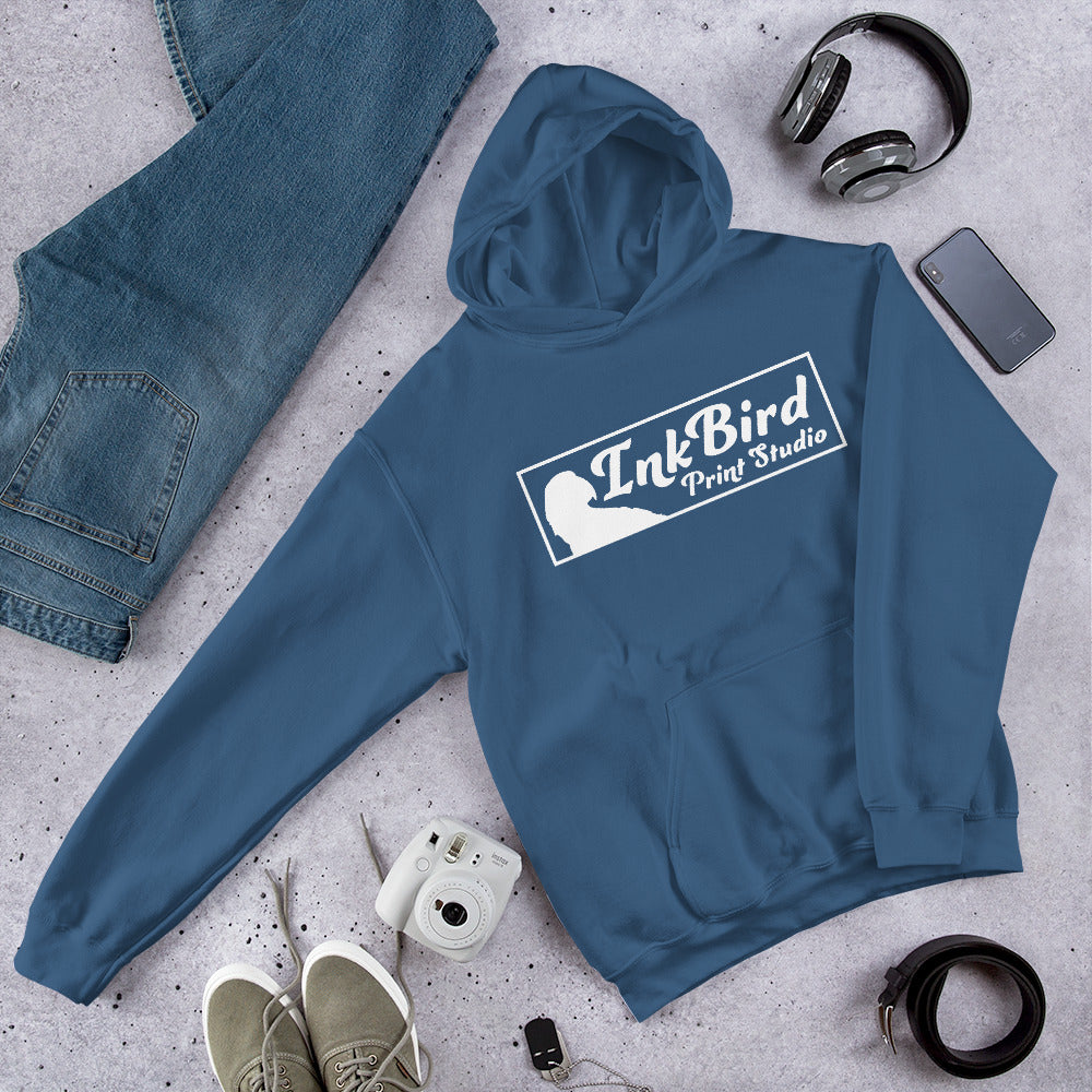The InkBird Print Studio Unisex Hoodie from InkBird Print Studio LLC, in a cozy blue design, is displayed on a cement surface. Surrounding it are stylish jeans, a camera, headphones, green sneakers, and a smartphone equipped with white earphones. This hoodie provides a soft feel that beautifully complements the modern accessories.