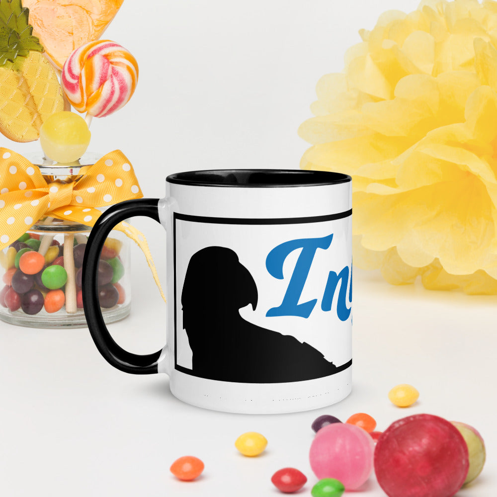An InkBird Print Studio Logo Mug with Color Inside from InkBird Print Studio LLC sits on a table surrounded by colorful candies. The mug, featuring a white ceramic body with a black handle, displays a silhouette of a person and the word "In" in blue. Nearby is a jar of sweets adorned with a yellow ribbon and large yellow flower decoration, offering both charm and dishwasher-safe convenience.